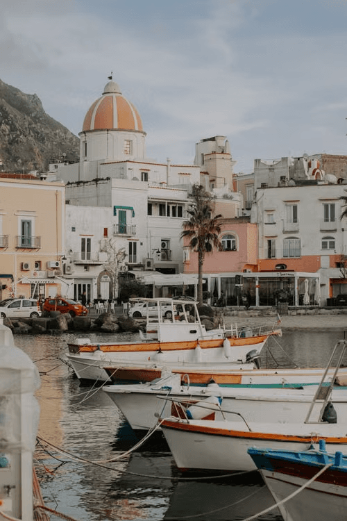 Small boats in an Ischia harbour beneath pastel waterfront buildings.
